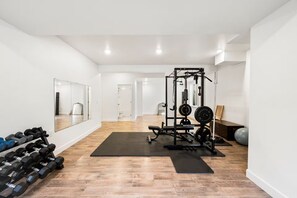 A spacious room with a wooden floor, a weightlifting station, and a mirror on one wall. - Sundance 2027 Retreat //4BR + Gym + 2-Car Garage (Superior)