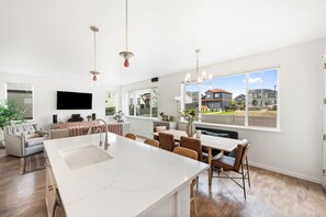 A spacious kitchen with a large island, dining area with chairs, a sofa, and a TV mounted on the wall. - Sundance 2027 Retreat //4BR + Gym + 2-Car Garage (Superior)