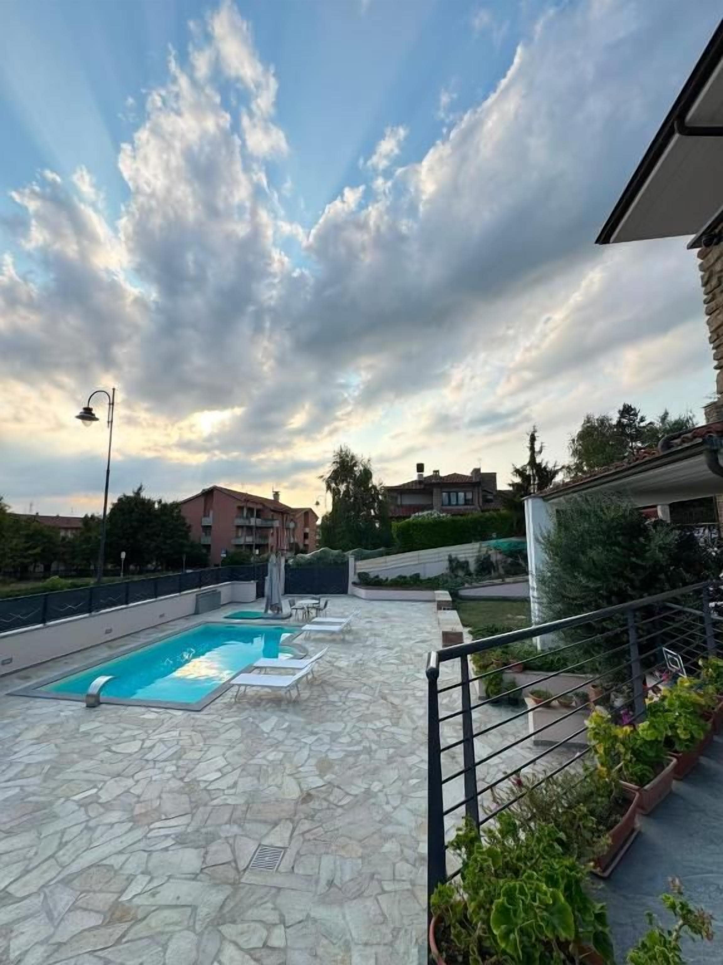 An outdoor swimming pool with lounge chairs, surrounded by stone flooring and potted plants.
