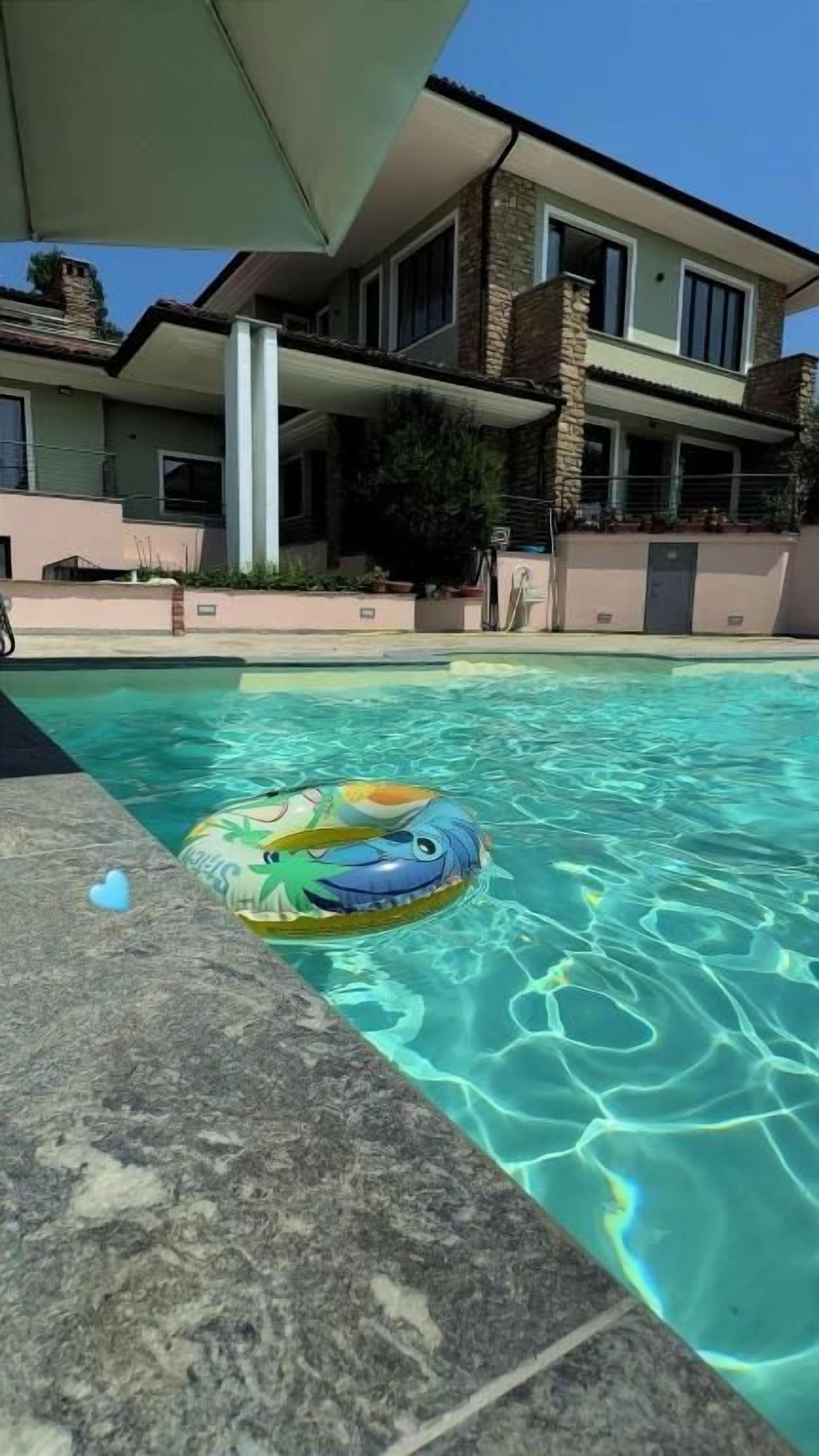 A swimming pool with clear water, a floating ring, and a building with a balcony in the background.
