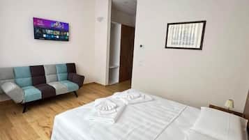 A hotel room with a bed, a sofa, a wall-mounted TV, and a door leading to another room.