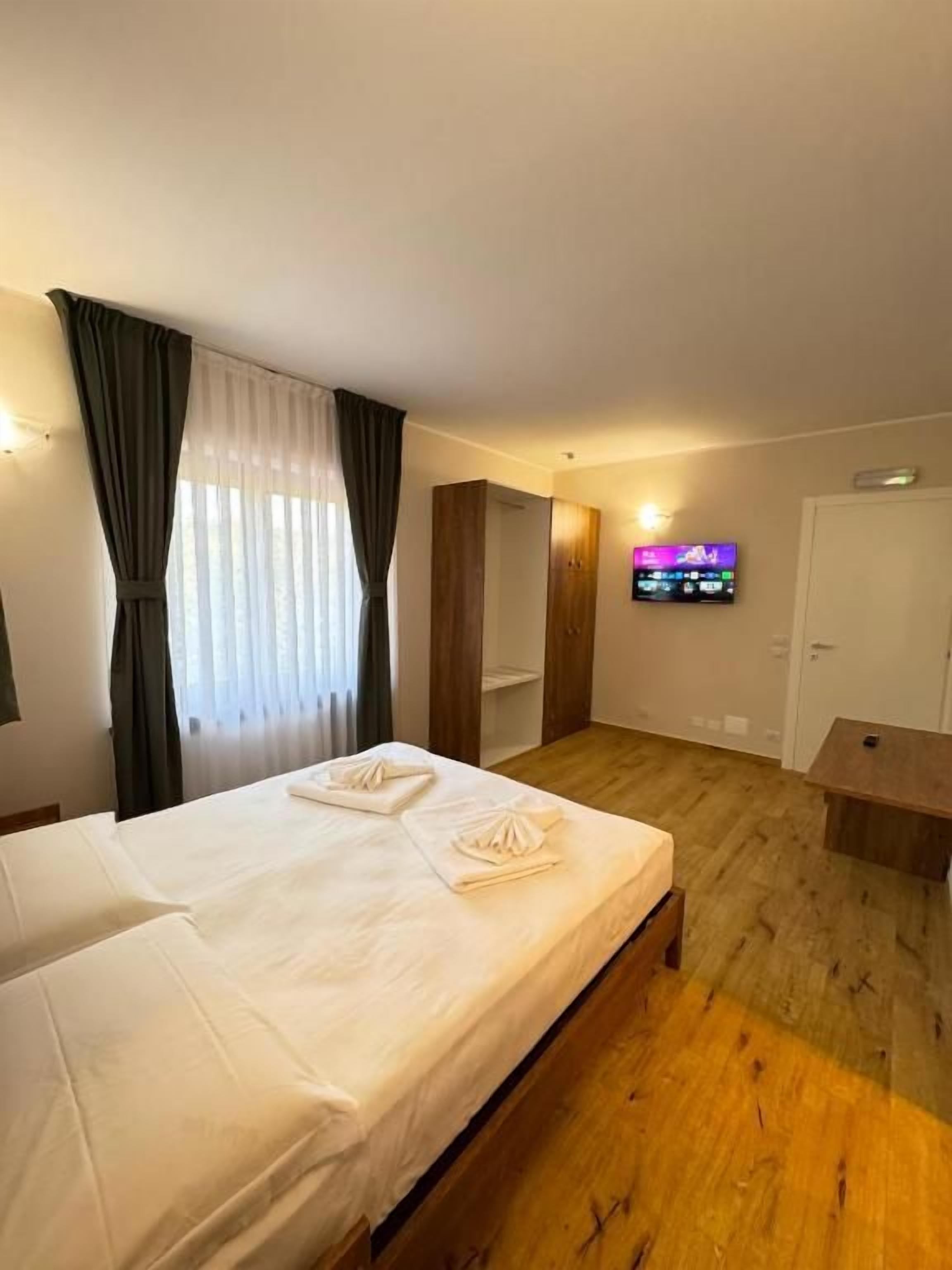 A hotel room with a bed, a TV, a wooden floor, and a wardrobe.