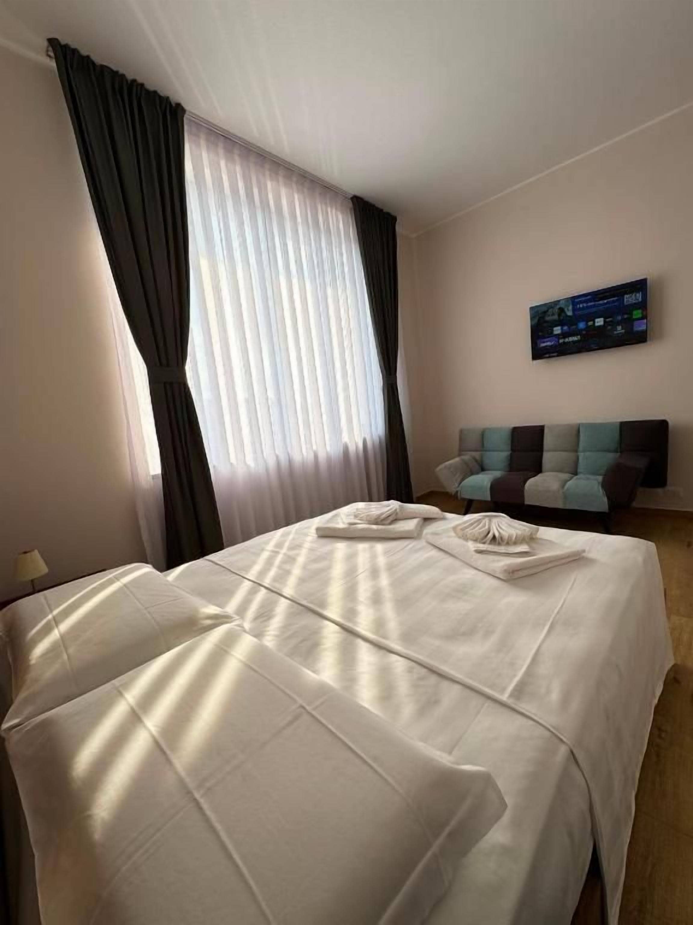 A hotel room with a bed, a flat-screen TV, a sofa, and a window with curtains.