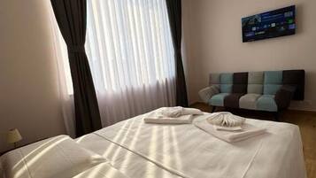 Une chambre d’hôtel équipée d’un lit, d’un téléviseur à écran plat, d’un canapé et d’une fenêtre avec des rideaux.