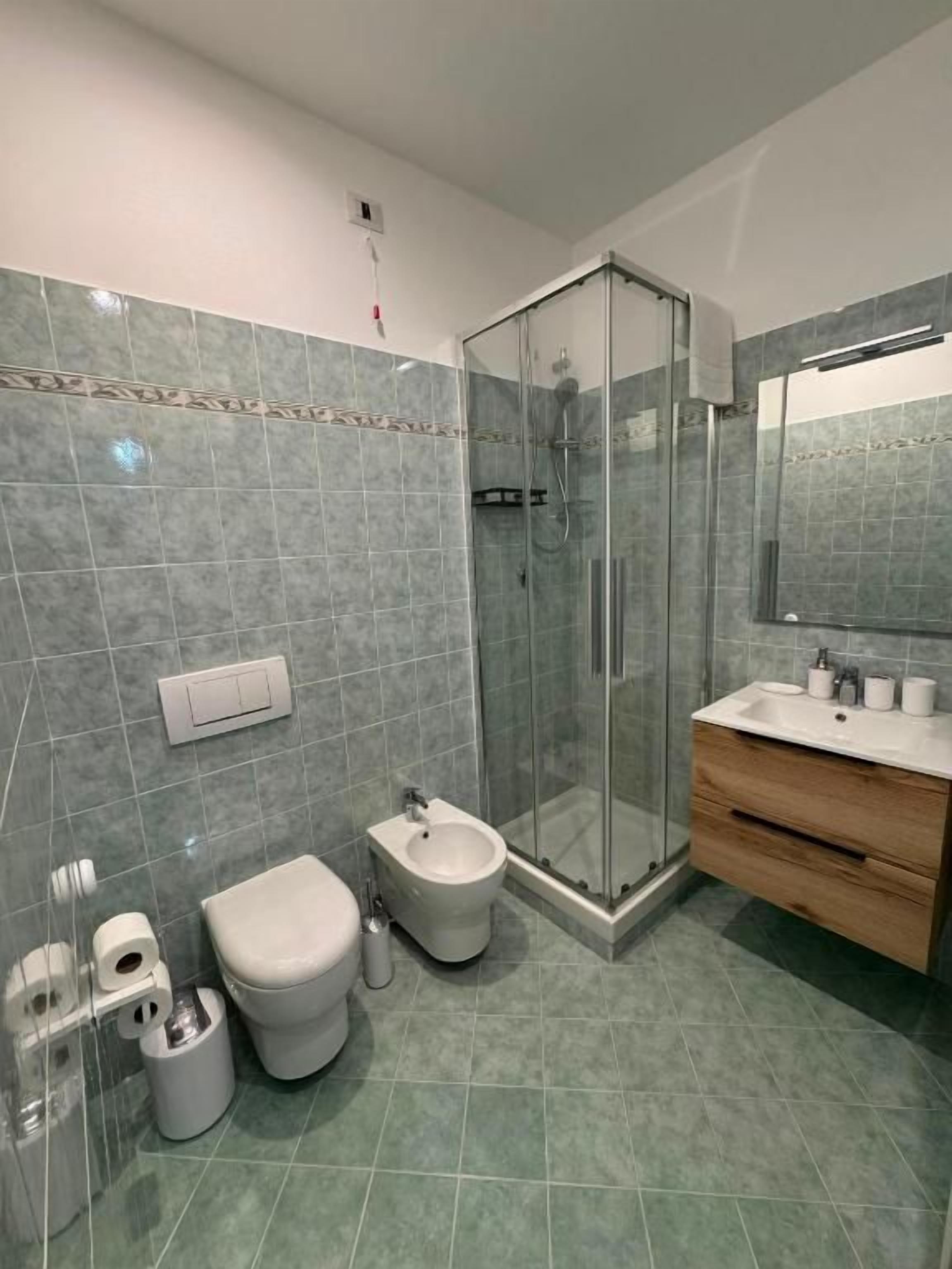 Un baño moderno con cabina de ducha de vidrio, un bidé, un inodoro y un lavabo con espejo.