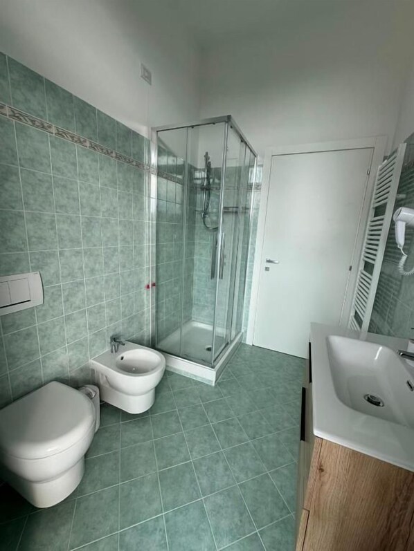 A bathroom with a glass shower enclosure, a toilet, bidet, and a sink.