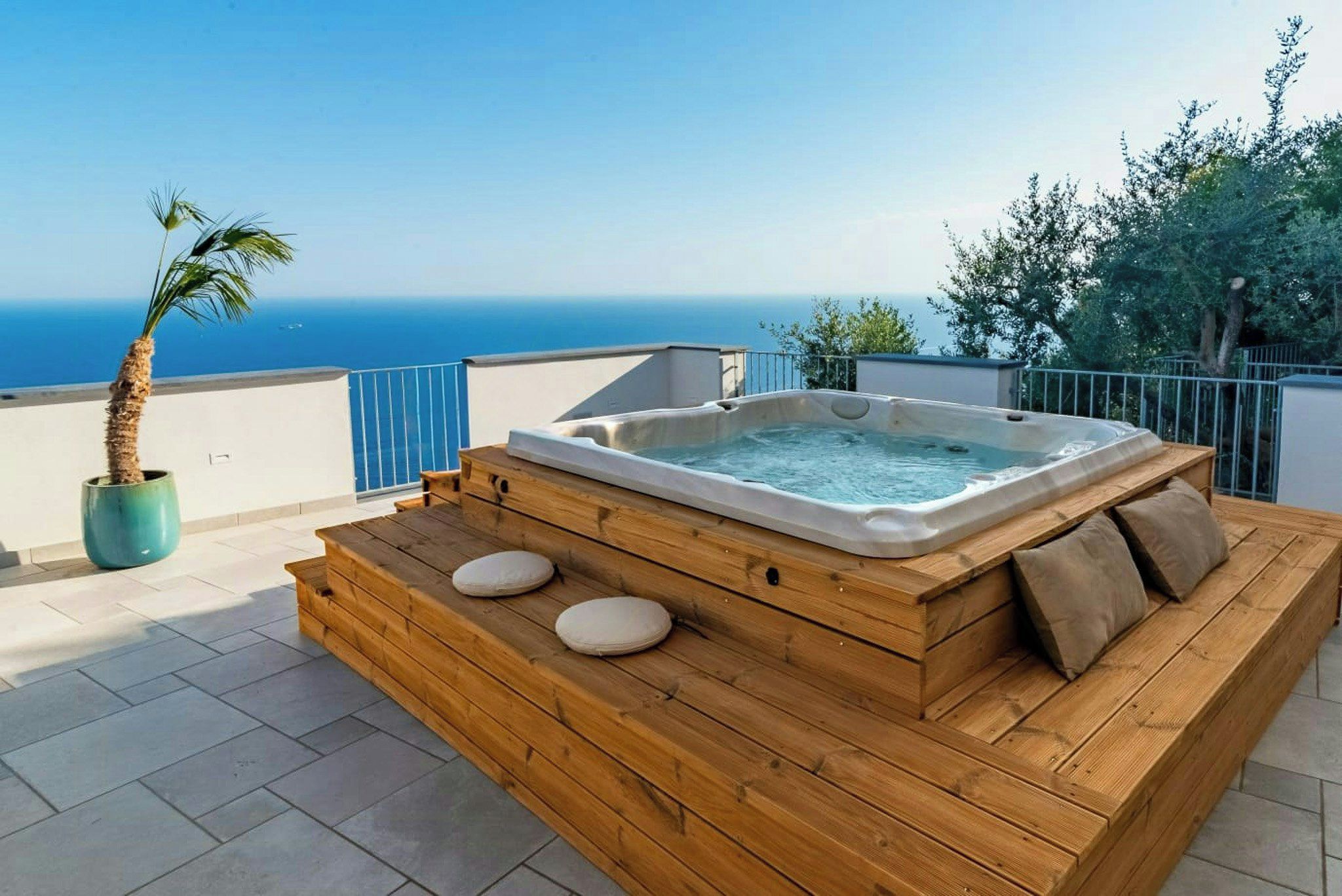 A wooden deck with a hot tub, a palm tree, and a view of the sea.