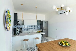 A modern kitchen with white cabinets, a stainless steel refrigerator, and a dining area with a wooden table and bar stools. - Villa with views over the Amalfi Coast and jacuzzi (Furore)