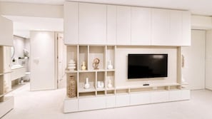 A modern living room with a large flat-screen TV, built-in shelving, and a minimalist design. - Victoria Levanco Apt by TrulyCyprus (Lemesos)