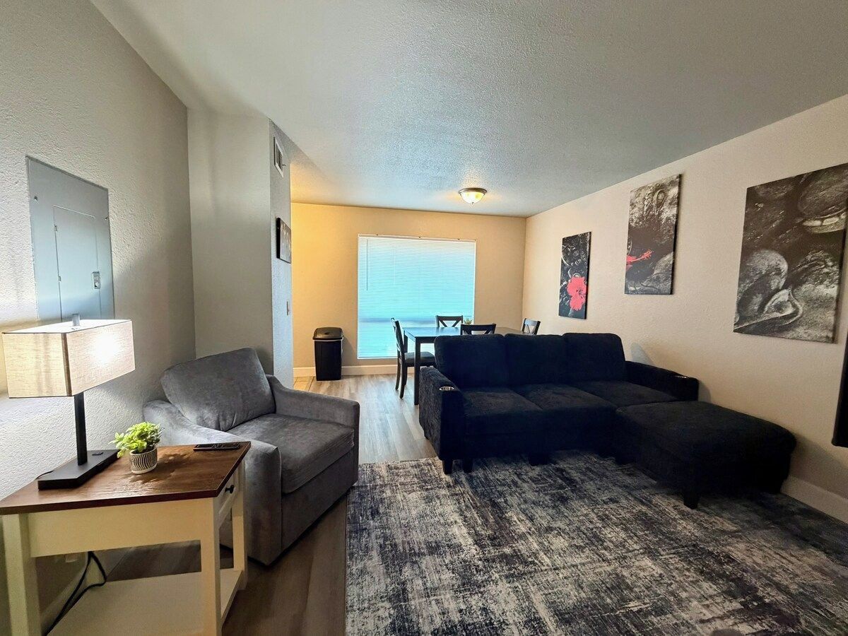 A living room with a sofa, a coffee table, a TV, and a window with blinds.