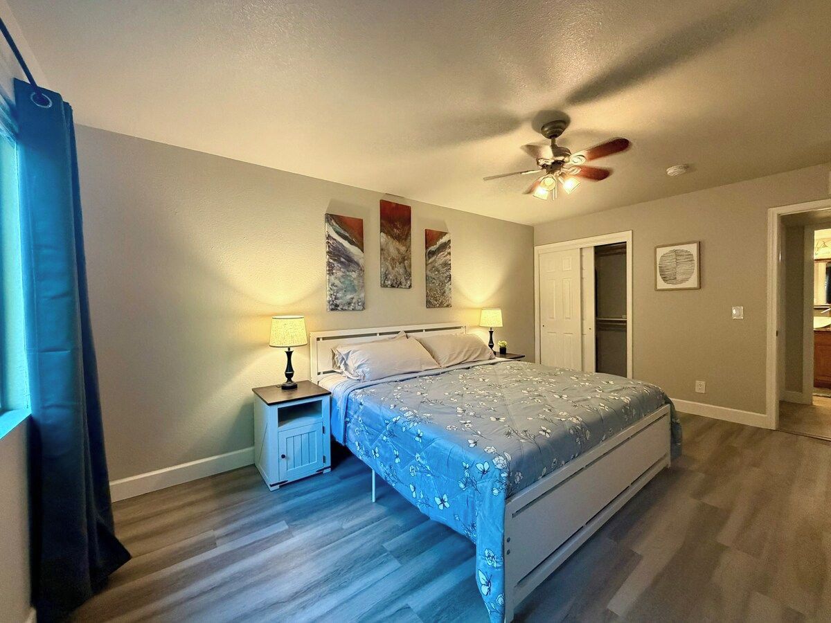 A bedroom with a bed, nightstands, a ceiling fan, and artwork on the wall.