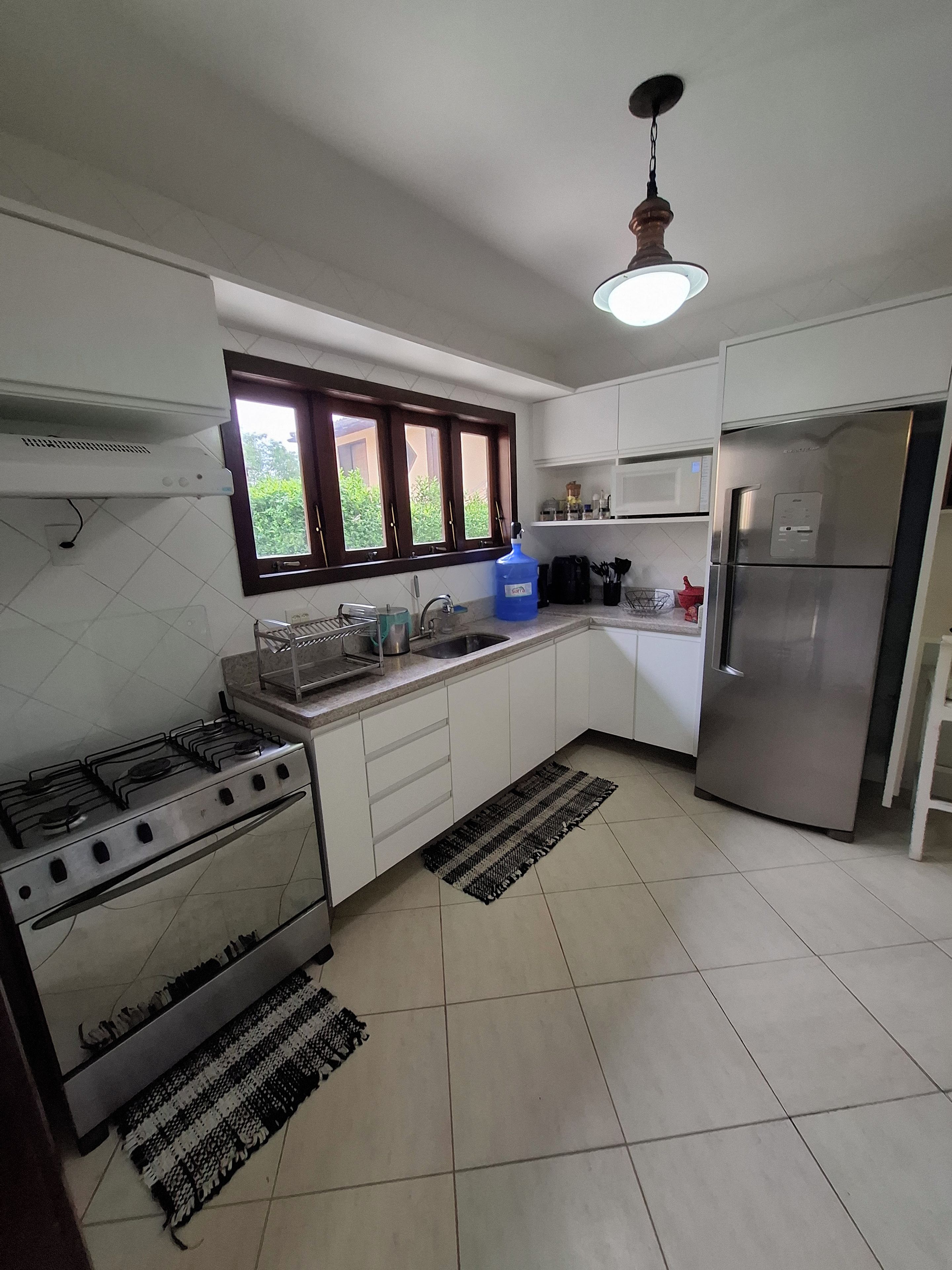 A kitchen with a gas stove, a refrigerator, a microwave, and a window with a view of greenery.