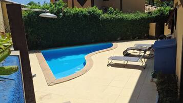 Ein Pool mit geschwungener Kante, umgeben von einer gefliesten Terrasse mit Liegestühlen.