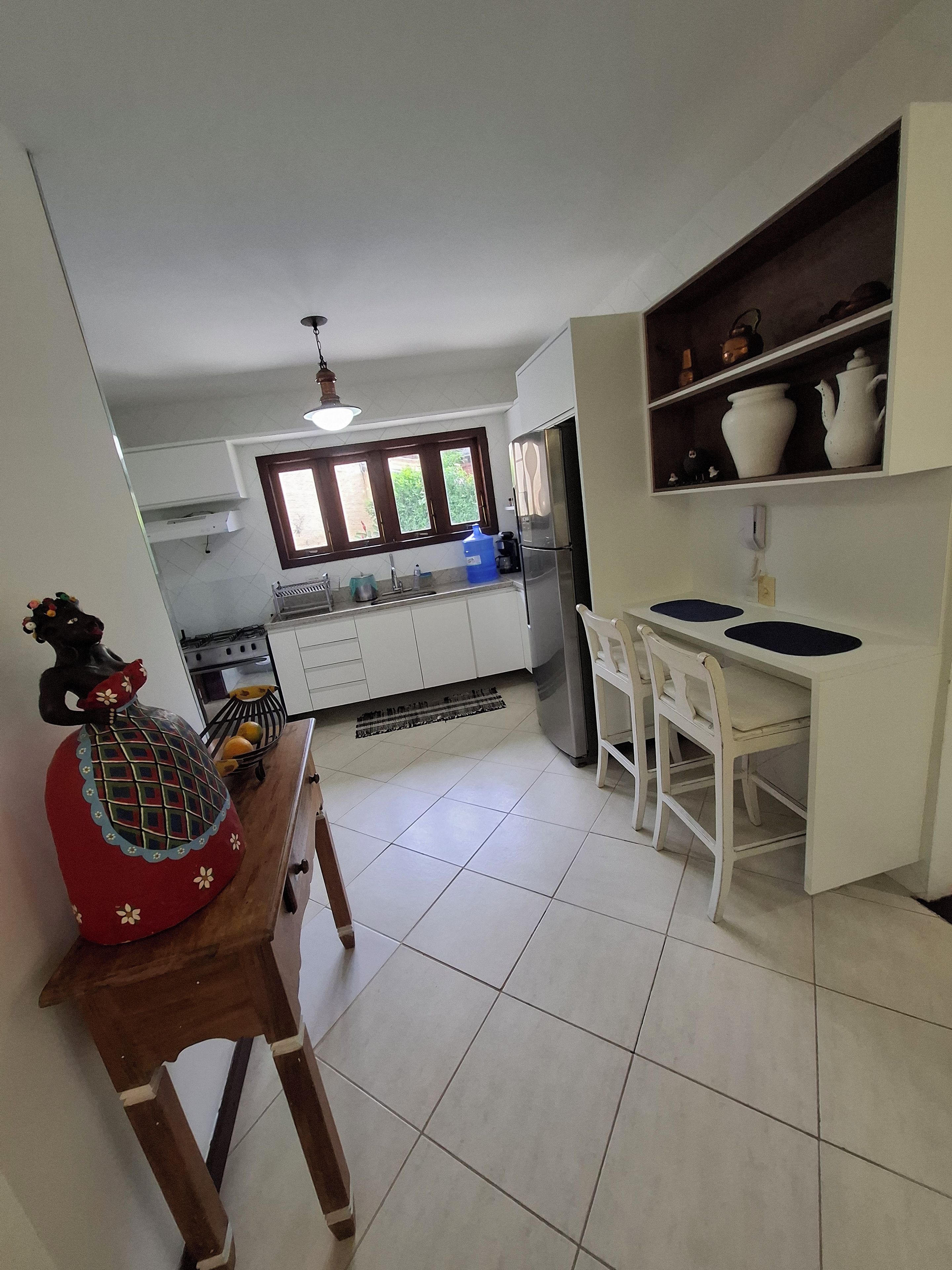 A kitchen with a refrigerator, sink, and window. There is a dining table with chairs and a decorative item on the table.