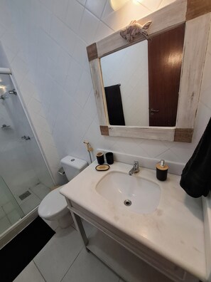 Een badkamer met een witte wastafel, een spiegel, een handdoekhouder, een toilet en een douche.