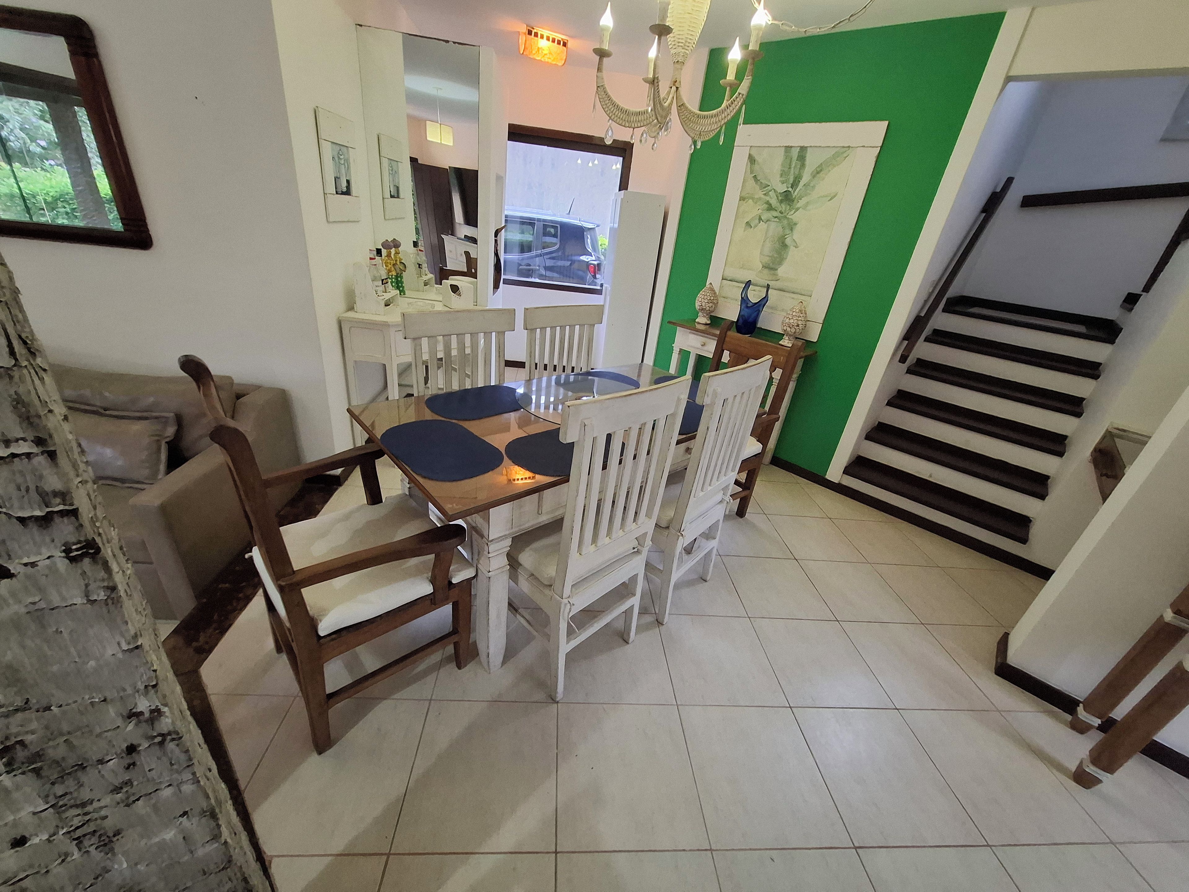 A dining area with a glass table and wooden chairs, a staircase, and a green accent wall.