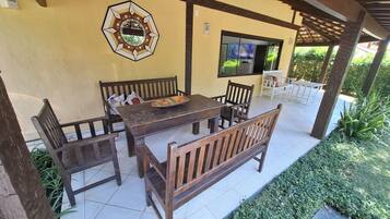 Ein überdachter Patio-Bereich mit Holztisch und Bänken, einem dekorativen Wandelement und einem Fernsehbildschirm.