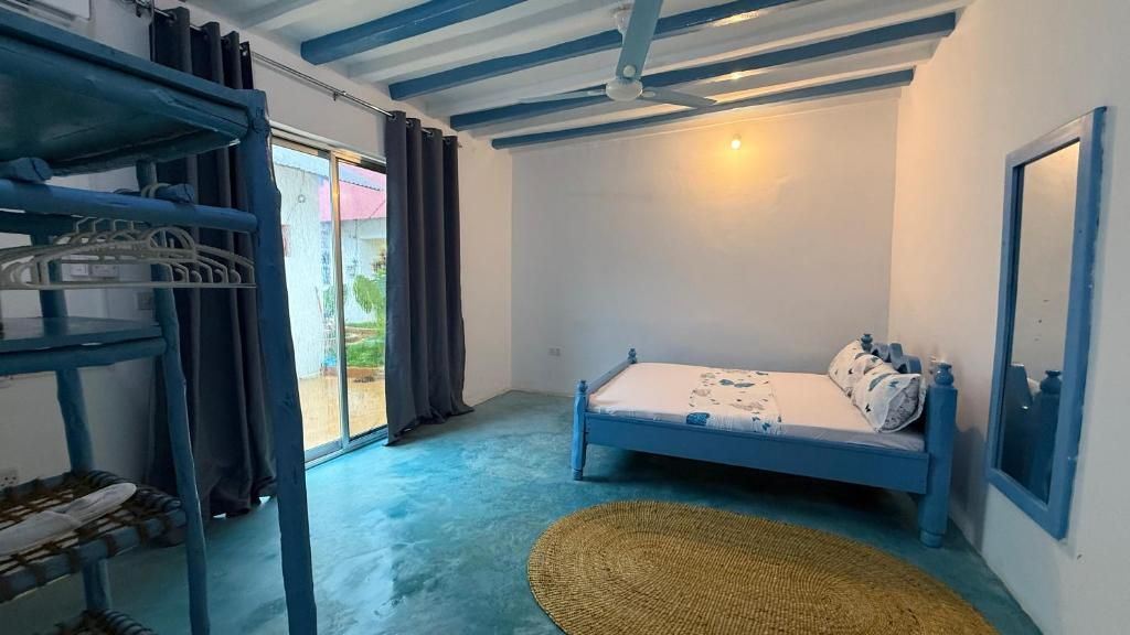 A bedroom with a bed, a bunk bed, a woven mat, and a sliding glass door leading to an outdoor area.