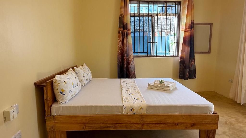 A single-bed room with a wooden frame, a white mattress, and a bedside table with a folded white cloth.
