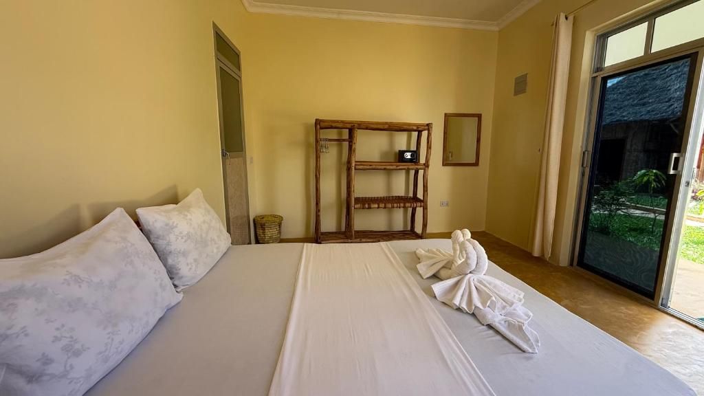 Une chambre d’hôtel avec un grand lit, une étagère en bois et une vue à travers une porte vitrée.