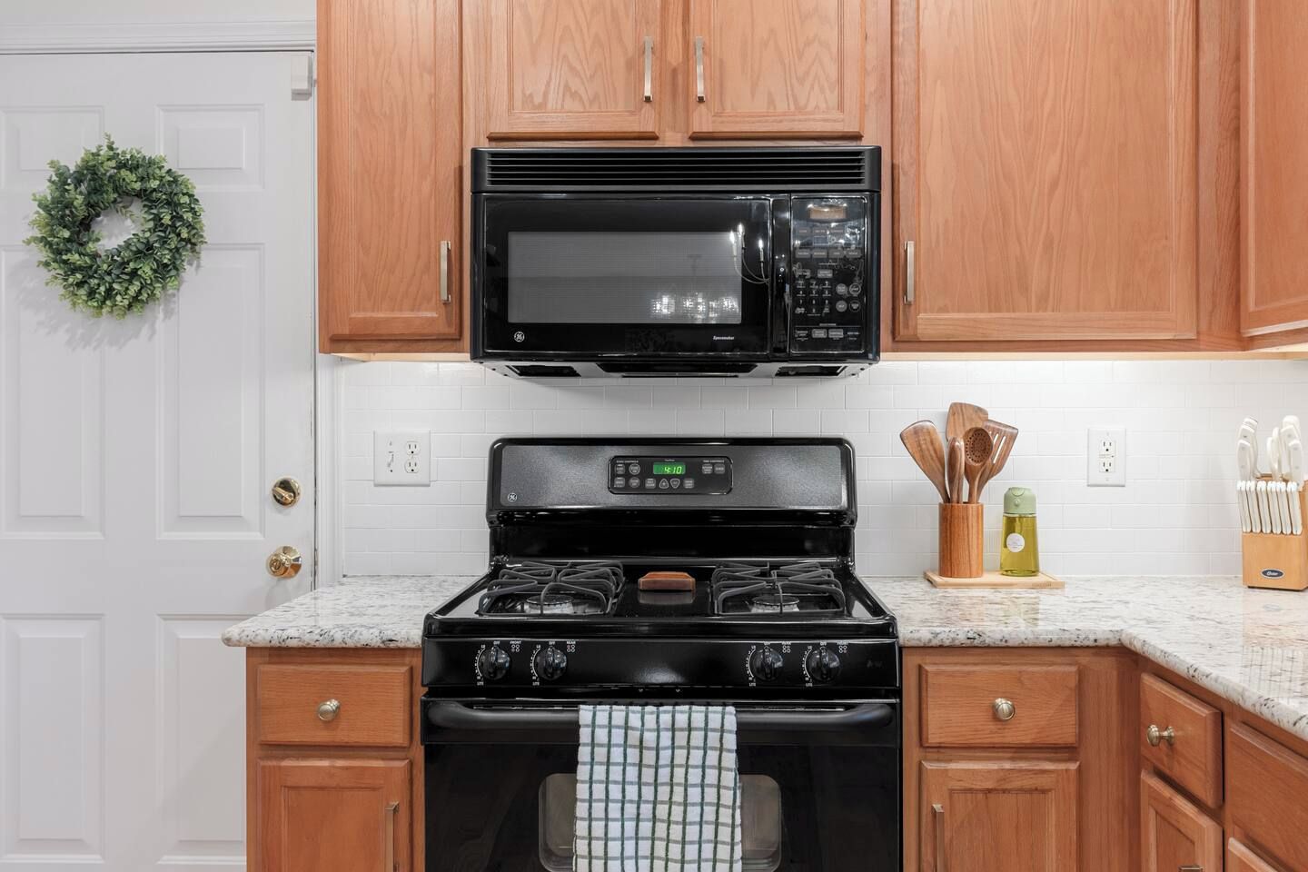 Una cocina con armarios de madera, una estufa negra, un microondas y una puerta blanca con un adorno navideño verde.