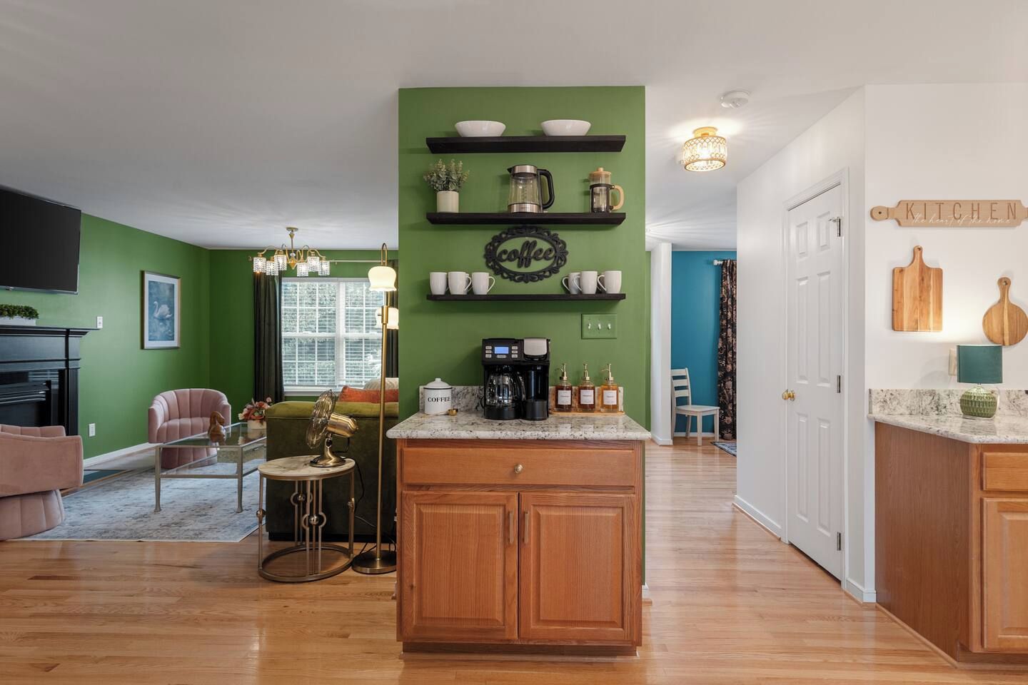 A modern kitchen with green walls, wooden cabinets, and a coffee station.