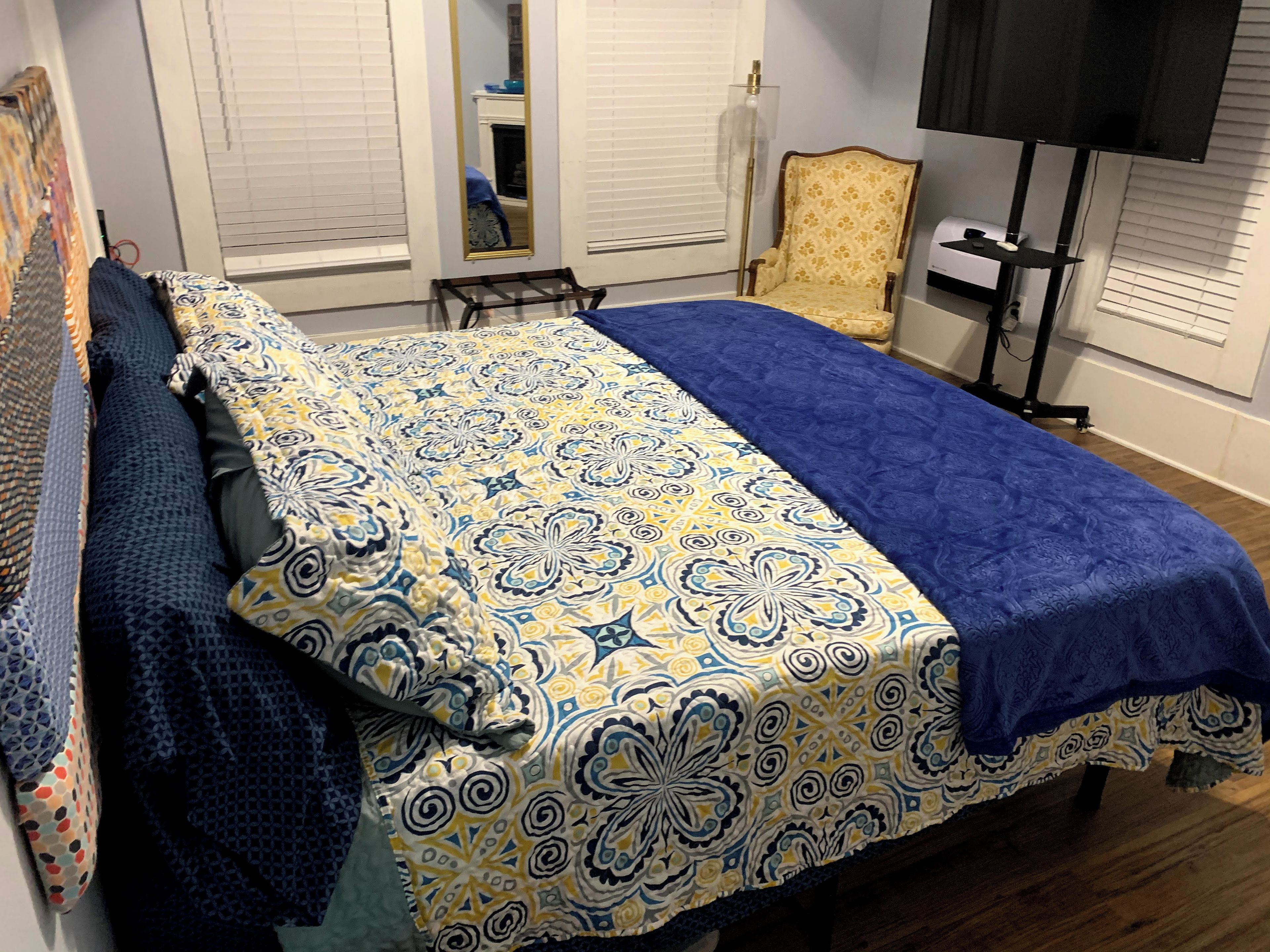 A bedroom with a bed, a chair, a television, and a window with blinds.
