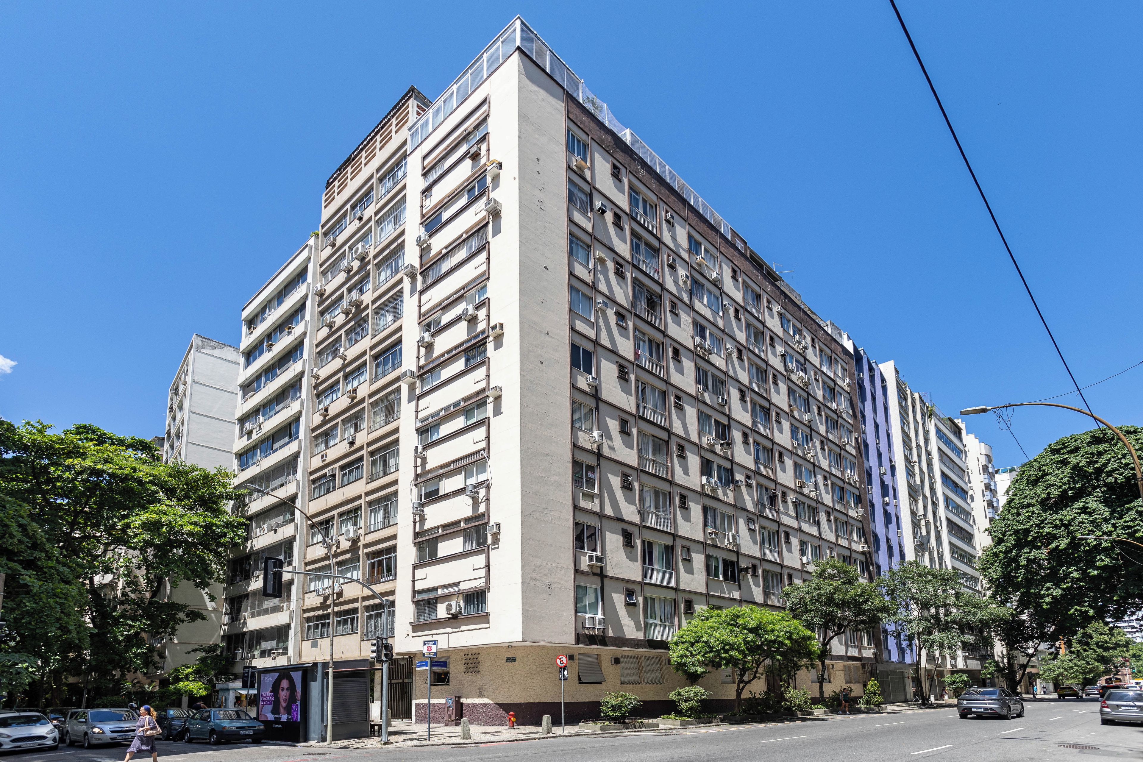 Un edificio residencial de varios pisos con balcones, un hidrante y una calle con coches y peatones.