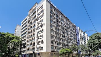 Un edificio residencial de varios pisos con balcones, un hidrante y una calle con coches y peatones.
