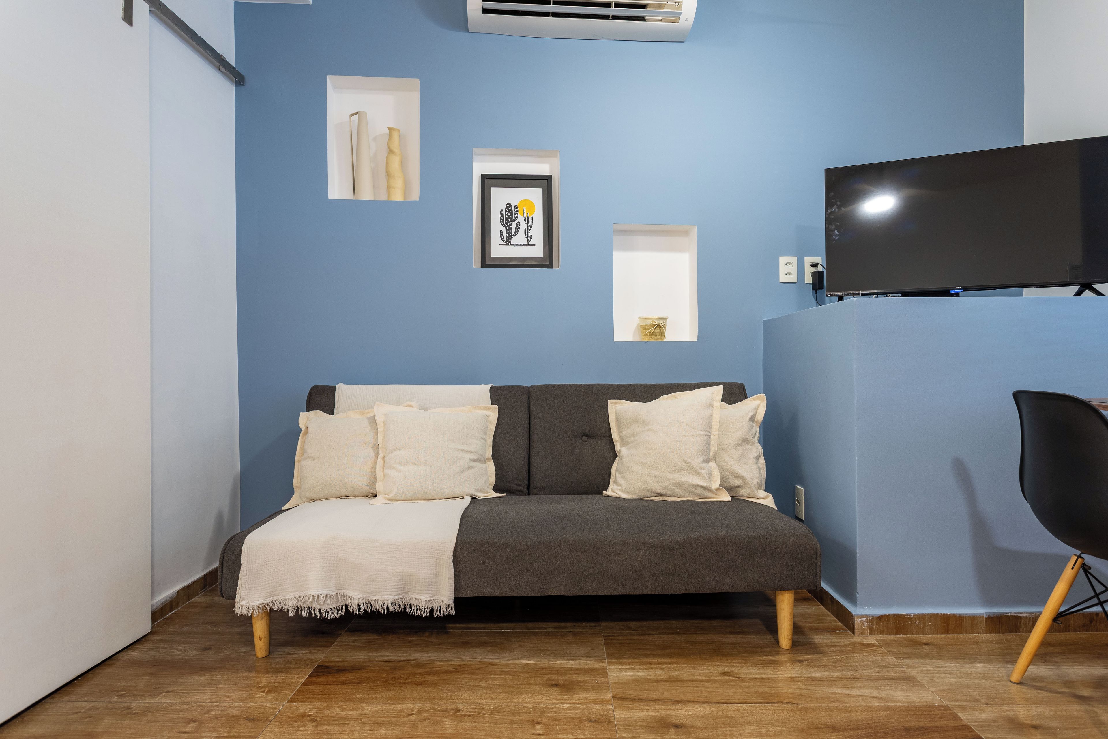 Una habitación con un sofá gris, un sillón negro, un televisor de pantalla plana y obras de arte en la pared.