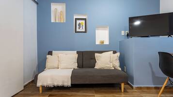 Una habitación con un sofá gris, un sillón negro, un televisor de pantalla plana y obras de arte en la pared.