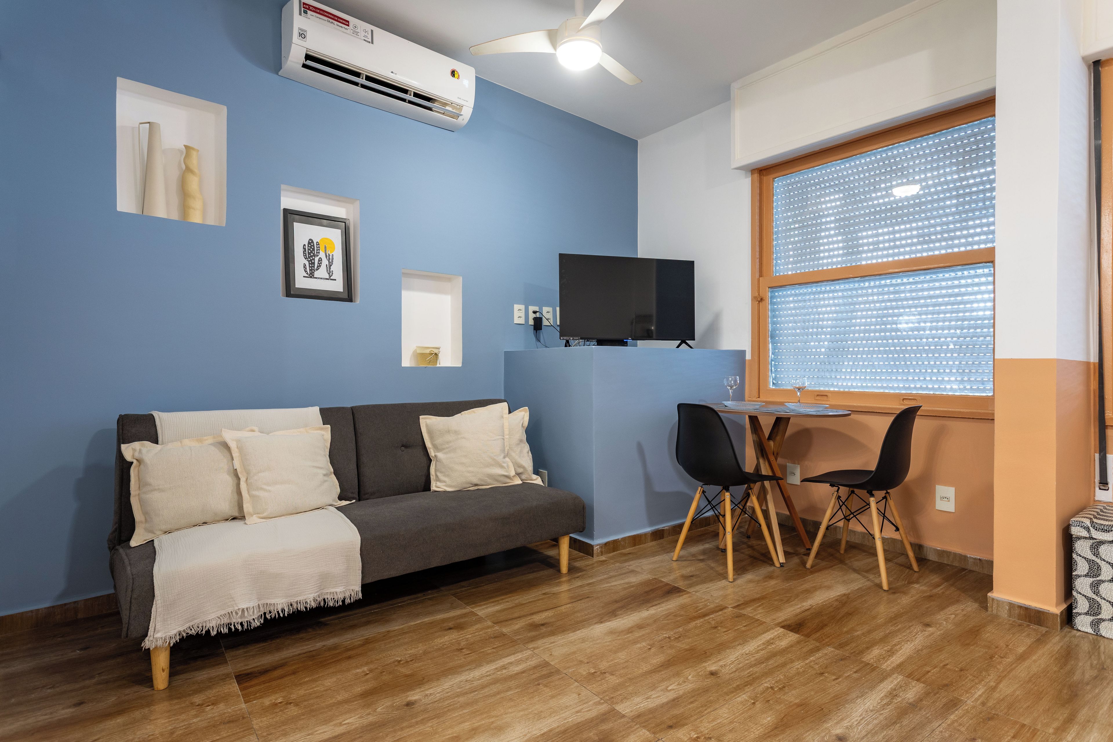 A room with a sofa, a TV, a small table, and a window with blinds.