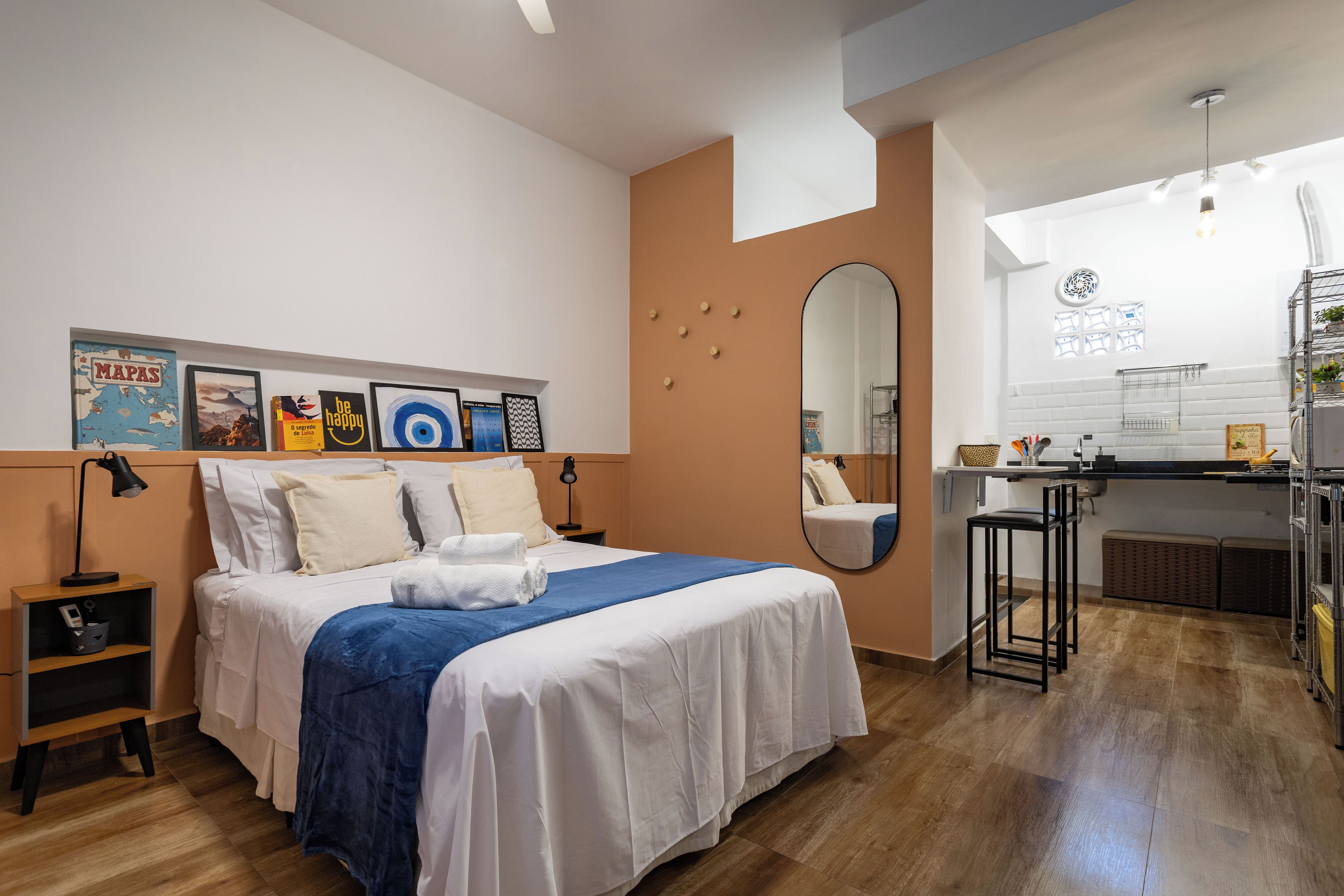 Una habitación de hotel moderna con una cama grande, un escritorio pequeño, un espejo y una kitchenette.