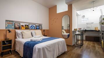 Una habitación de hotel moderna con una cama grande, un escritorio pequeño, un espejo y una kitchenette.