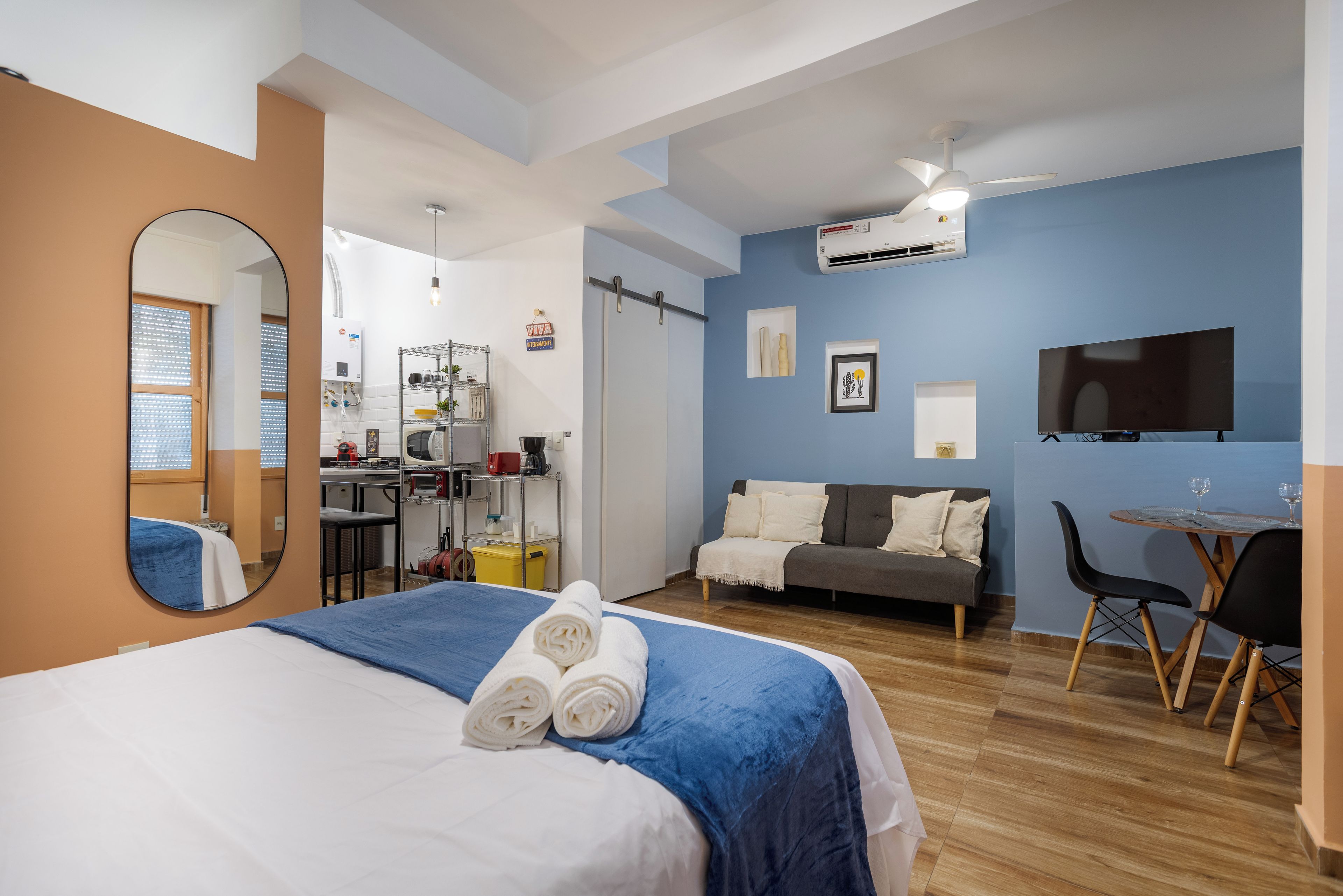 Una habitación de hotel con cama, escritorio, silla, televisión y kitchenette.