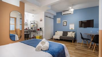Una habitación de hotel con cama, escritorio, silla, televisión y kitchenette.