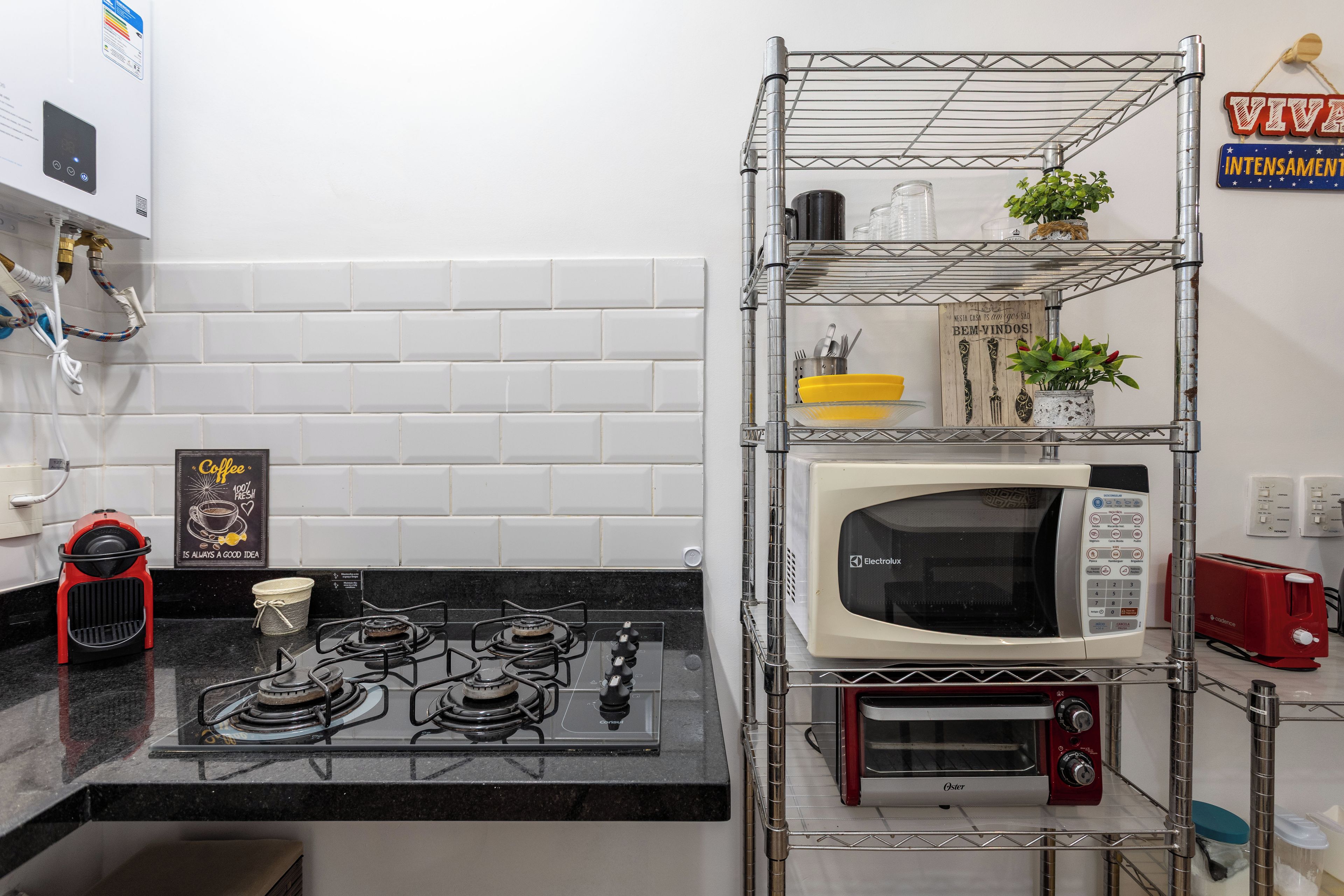 Eine kompakte Küche mit einem Gasherd, einer Mikrowelle, einem Toaster und einem Metallregal mit Küchenutensilien.