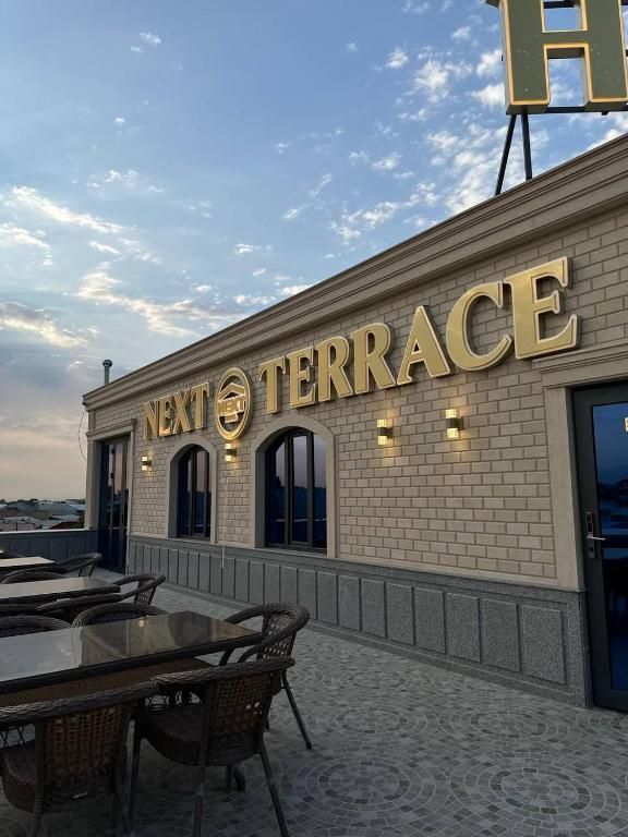 Un edificio con un letrero que dice 'NEXT TERRACE' y asientos al aire libre con mesas y sillas.