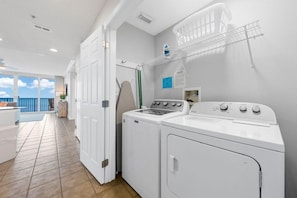 A laundry area with a washing machine and dryer, a drying rack, and a view of the ocean through a door. - San Carlos 1007 (Gulf Shores)