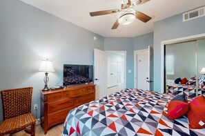 A bedroom with a bed, dresser, chair, ceiling fan, and a door. - San Carlos 1003 (Gulf Shores)