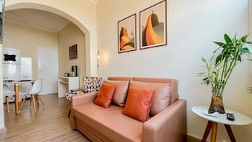 Ein Wohnzimmer mit einer Couch, einem Esstisch mit Stühlen, einer Pflanze und Kunstwerken an der Wand.
