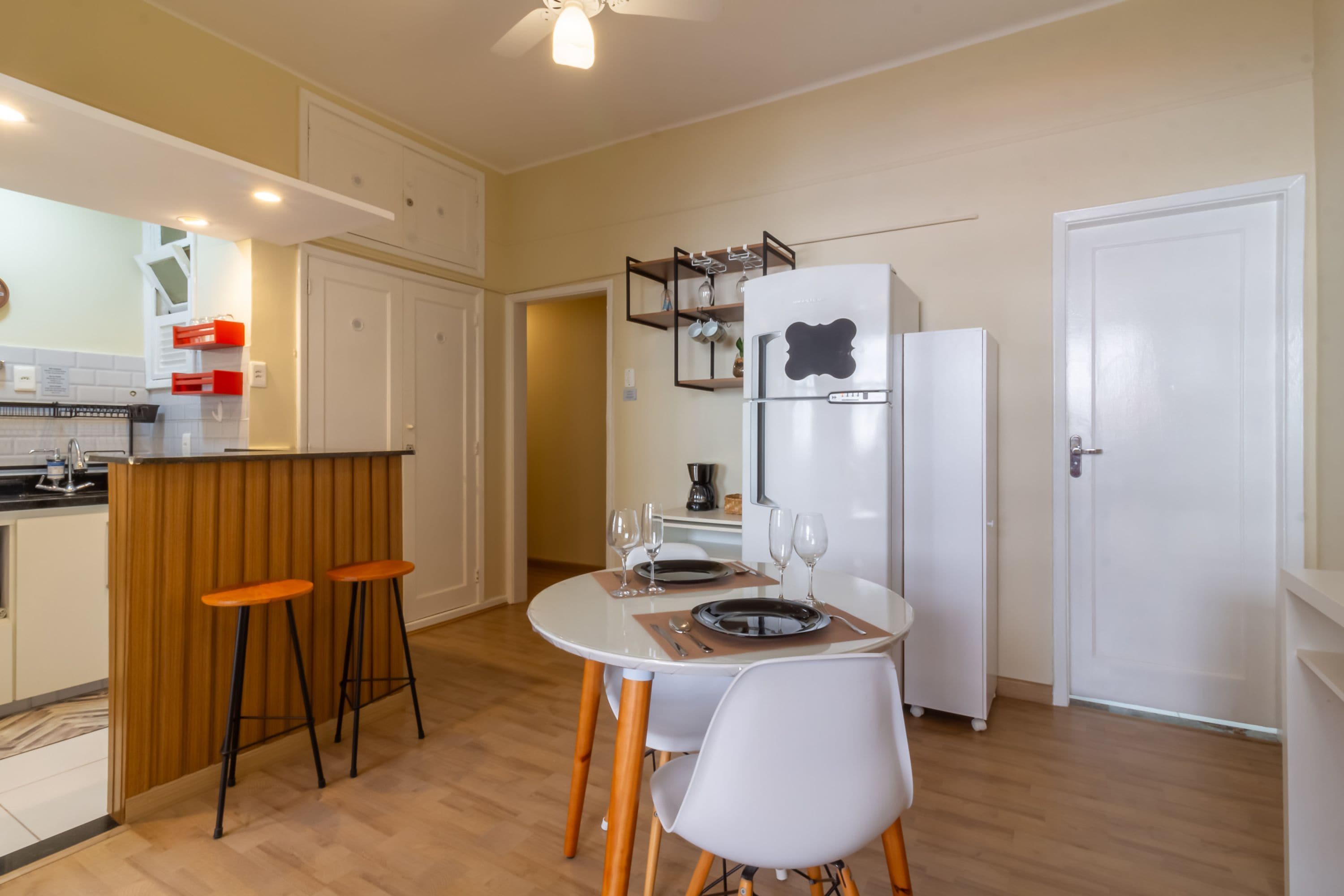 A compact kitchen with a white refrigerator, a wooden bar counter, and a dining table set for two.