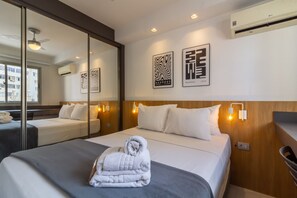 Una habitación de hotel con cama, espejo, obra de arte en la pared y ventilador de techo.