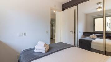 A hotel room with a bed, a bedside table, a mirror, and a door leading to another room.