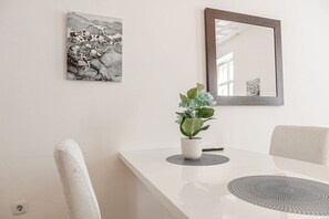 A dining area with a white table, two chairs, a potted plant, a mirror, and a wall-mounted artwork. - Bring Everyone 3BR near Belvedere Palace (Vienna)