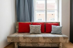 A corner sofa with a patterned fabric and three cushions, positioned in front of a window with a view of buildings. - Bring Everyone 3BR near Belvedere Palace (Vienna)