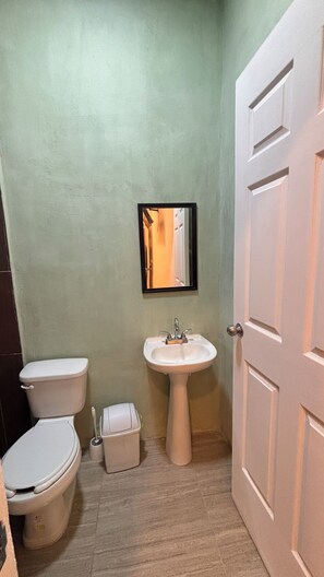 A bathroom with a toilet, sink, and a door. - Cozy 1-Bedroom Apartment with Pool in Chelem (Chelem)