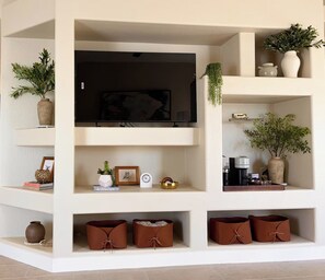 Un salon moderne avec un téléviseur à écran plat, des étagères ornées d’objets décoratifs et des plantes en pot.
