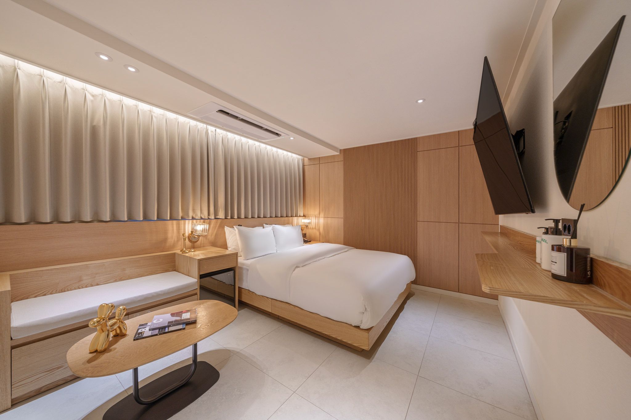 A modern hotel room with a bed, a sofa, a small table, and a TV.