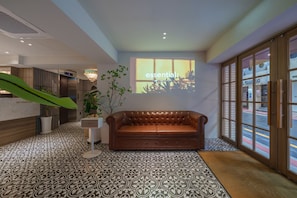 A lobby with a leather sofa, patterned floor tiles, a reception desk, and a projection screen displaying 'essential:' - Browndot Hongdae Sinchon (Seoul)